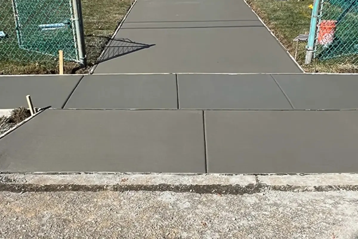 Freshly poured gray concrete driveway with a jointed apron section meeting the sidewalk at the street