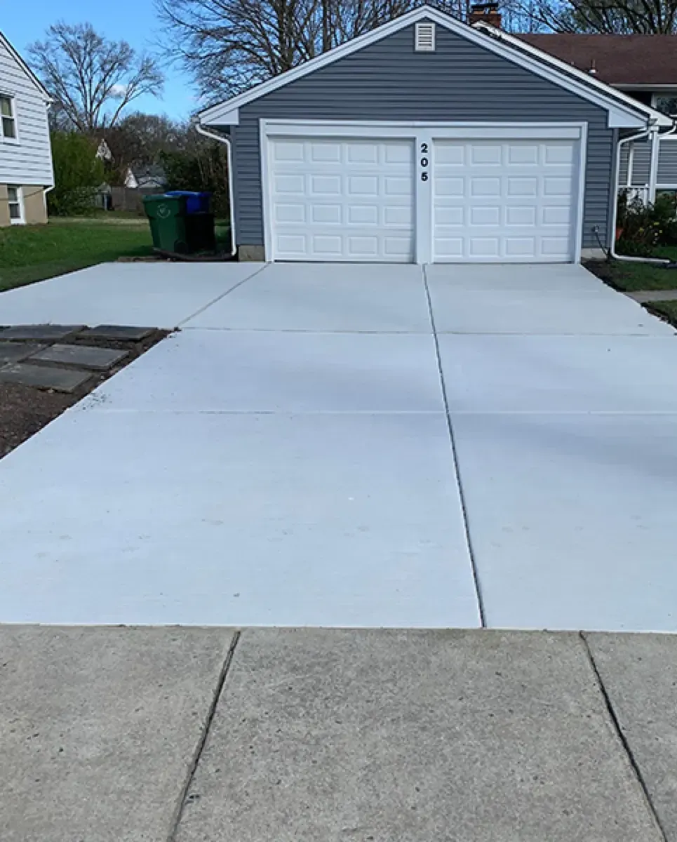 Finished light gray concrete driveway leading to a two-car garage with trimmed lawn edges on both sides